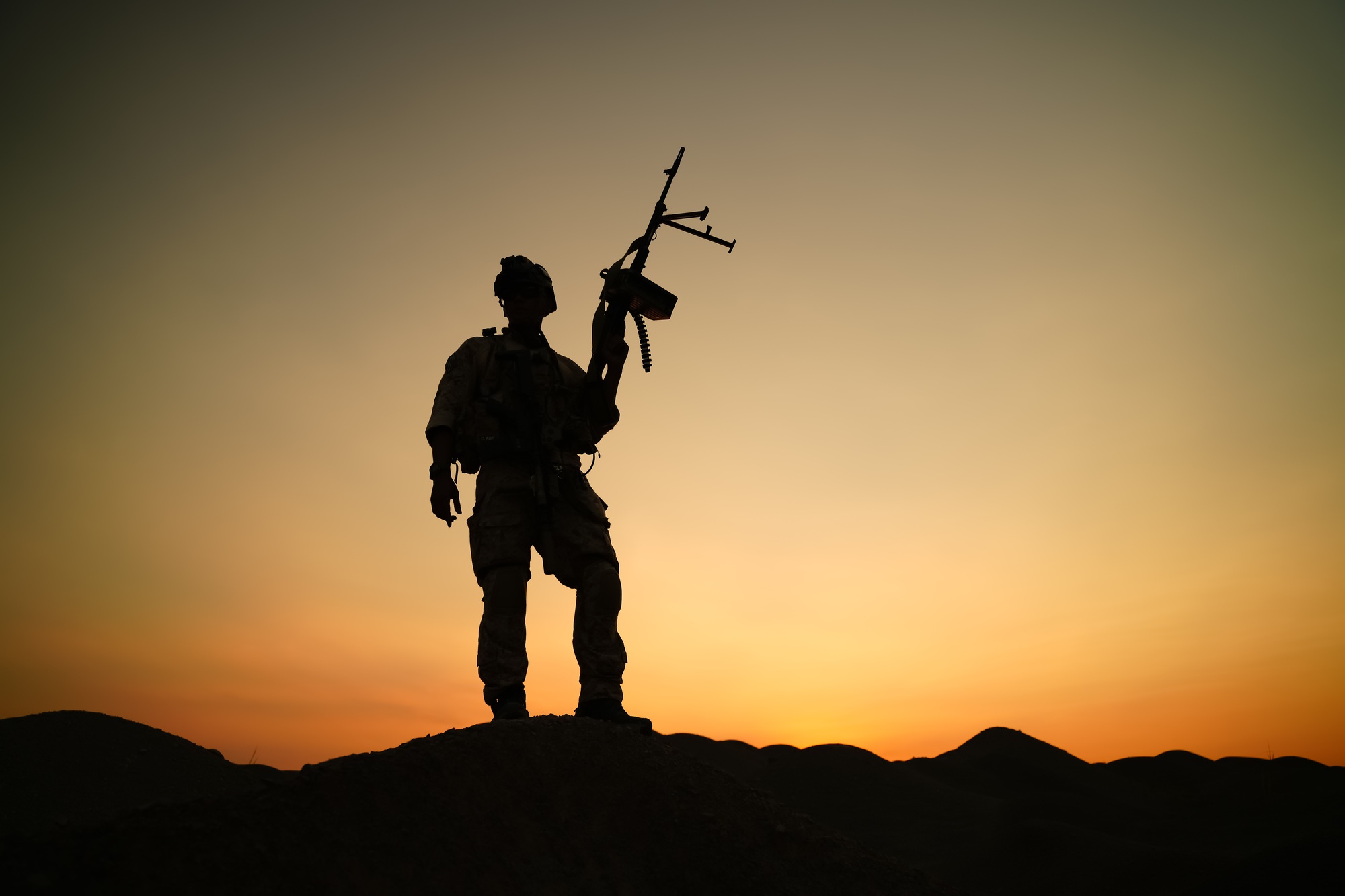 Soldier standing on hilltop with weapon at sunset in a dramatic silhouette